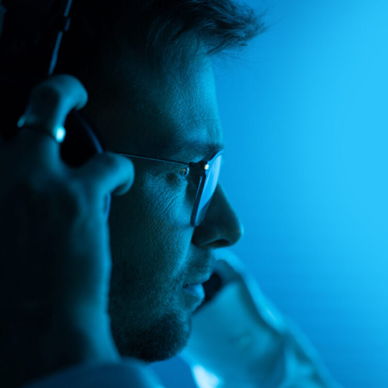 Caucasian Music Producer in His 30s Listening a Music Using Professional Headphones. Entertainment Industry. Dark Blue Illuminated Room.